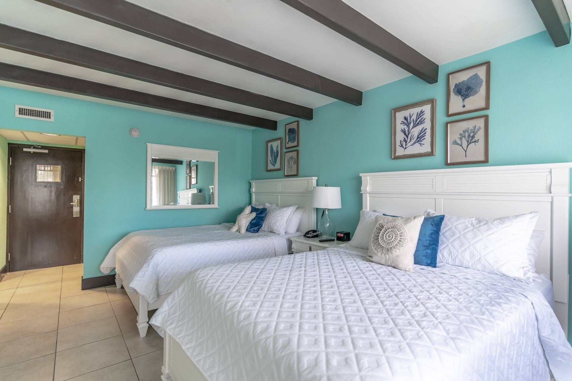 A hotel room with two beds, a large mirror, and artwork on the walls.