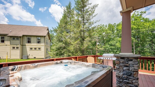 Ein Whirlpool auf einer Holzterrasse mit einem Steinpfeiler, einem Grill und einem Haus im Hintergrund.