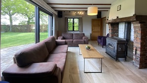 A spacious living room with a large window, a sofa, a coffee table, and a fireplace. - Holiday home surrounded by woods and meadows (Grote Brogel)