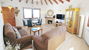 A living room with a sofa, a dining table with chairs, a fireplace, a television, and a cabinet. - Aaron - holiday home with stunning views and private pool in Calpe (Calpe)