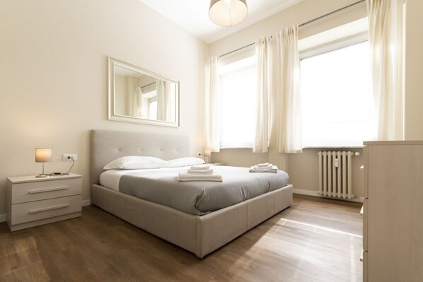 Una camera da letto moderna con un letto, un comodino, una lampada e un'ampia finestra con tende.