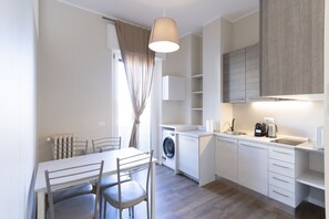 Una cocina compacta con lavadora, un comedor con sillas e iluminación colgante.
