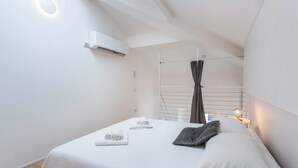 A modern bedroom with a bed, a wall-mounted air conditioner, a window with curtains, and a bedside table with a lamp. - Apartment "Varenna amorevole dimora in Lecco" with Air Conditioning (Lecco)