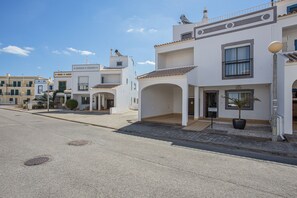 A street view of white buildings with balconies, a clear sky, and a paved road.