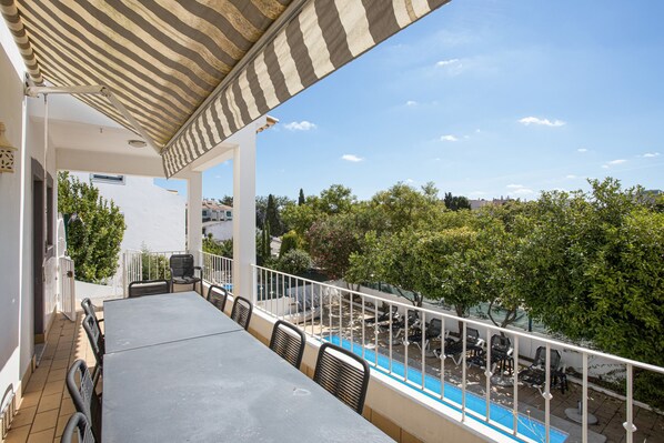 A covered outdoor area with a pool, chairs, and a view of trees and buildings.