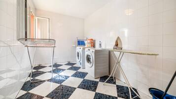 A laundry area with a washing machine, dryer, ironing board, and a mop bucket.