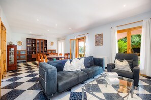 A living room with a checkered floor, a sofa, a glass coffee table, and a dining area with chairs and a table.