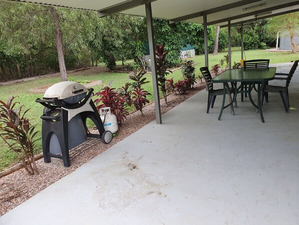 A covered patio area with a grill, a table with chairs, and a variety of plants. - Curlew Lodge -1 road back from beach. Limited WiFi is now available (Dundee Beach)