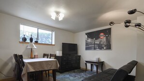 Ein Wohnzimmer mit Essbereich, einer schwarzen Couch, einem Fernseher und einem Poster an der Wand.