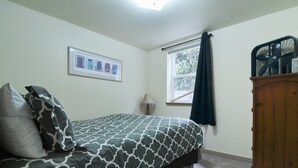 Ein Schlafzimmer mit einem Bett, einem Fenster mit Vorhängen, einer Lampe und einem Holzschrank.