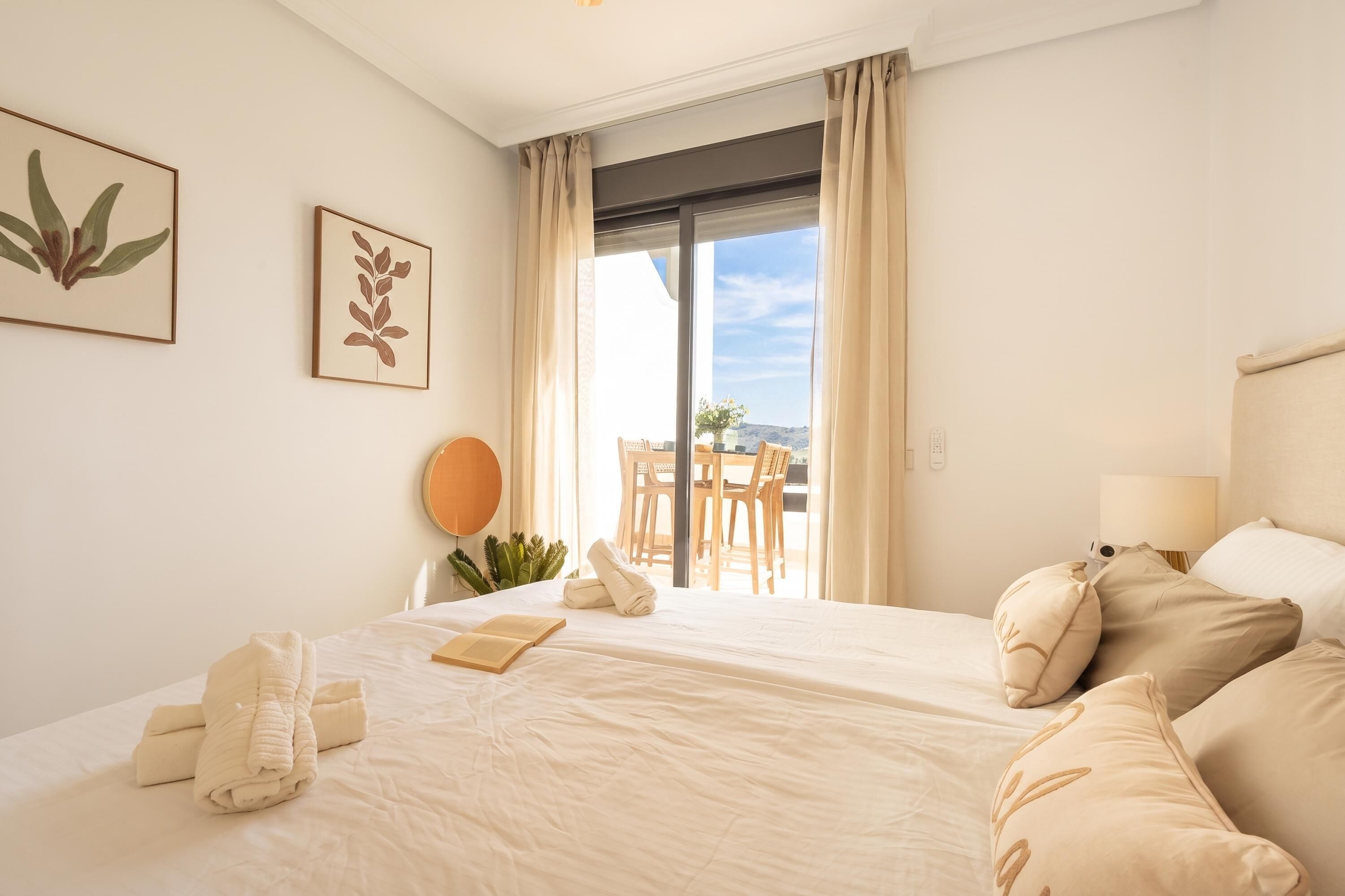 Una cama bien hecha con almohadas, una mesita de noche con una lámpara y una ventana con cortinas.