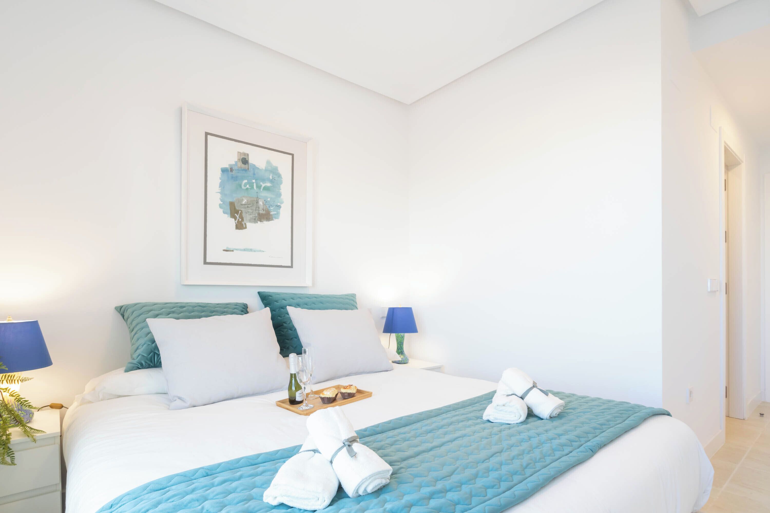 A neatly made bed with a blue quilt, white pillows, and a framed picture on the wall.