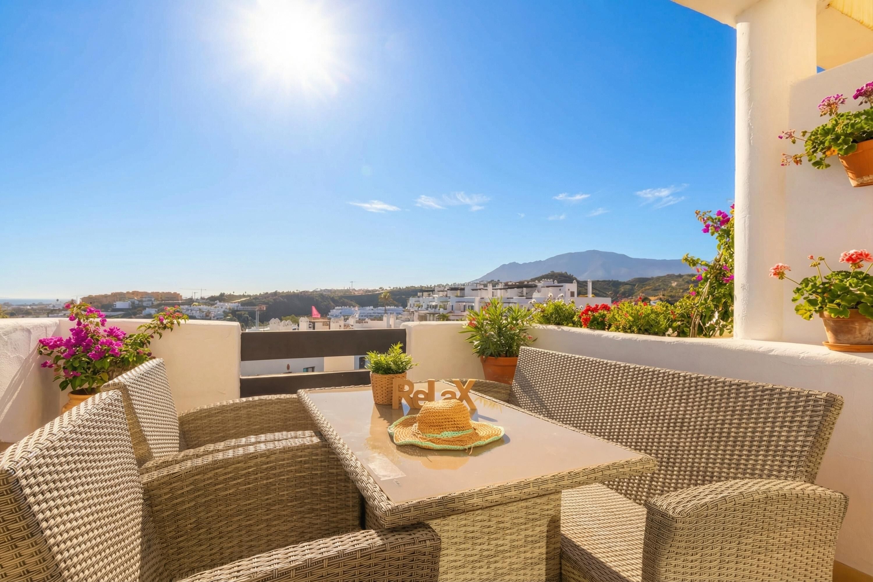 A wicker outdoor seating area with a table, potted plants, and a view of a cityscape and mountains.