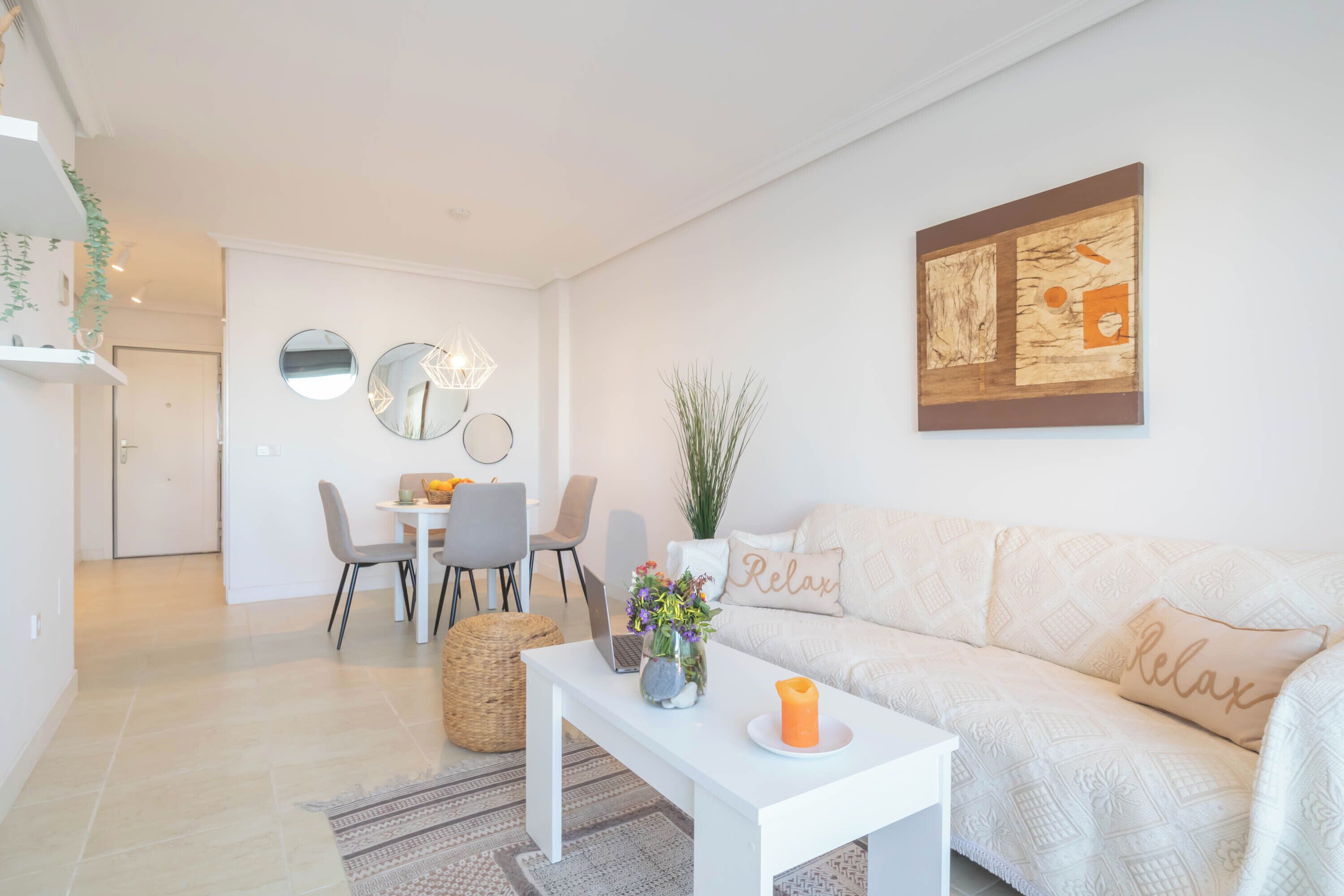 A modern living room with a white sofa, a coffee table, and a dining area with a white table and chairs.