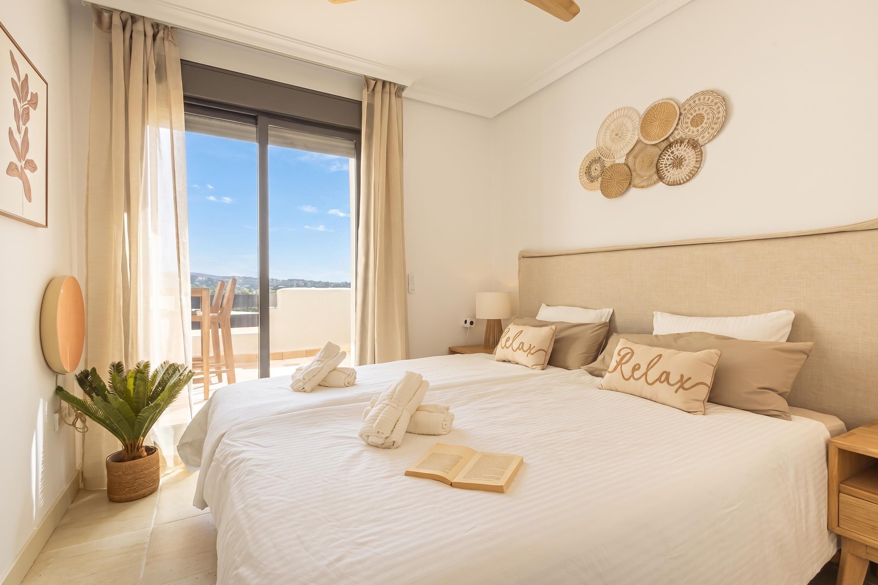Ein Hotelzimmer mit einem großen Bett, einer Topfpflanze, Blick durch eine Schiebetür und einem Wanddekor.