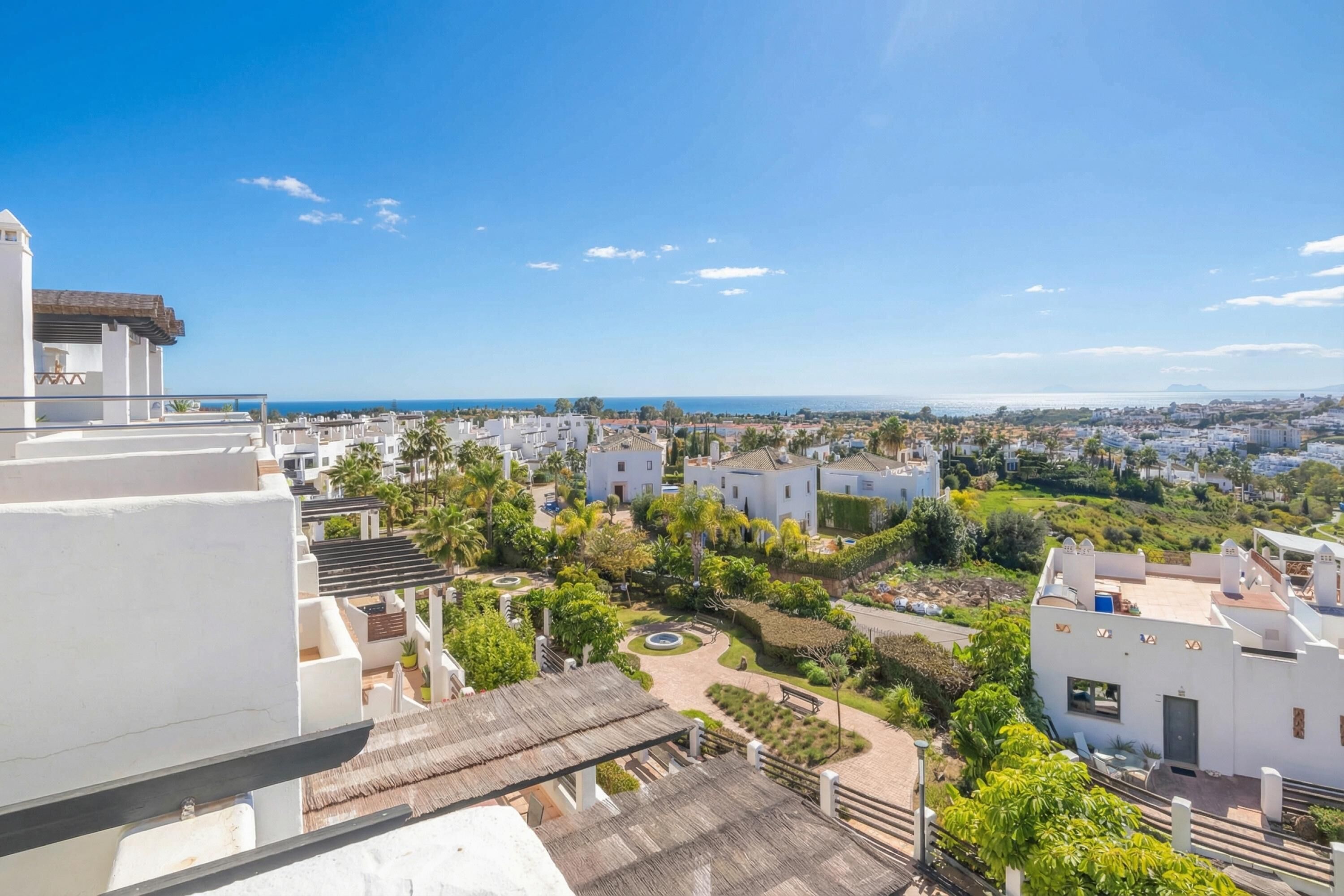 A residential area with white buildings, a clear blue sky, and a view of the sea.