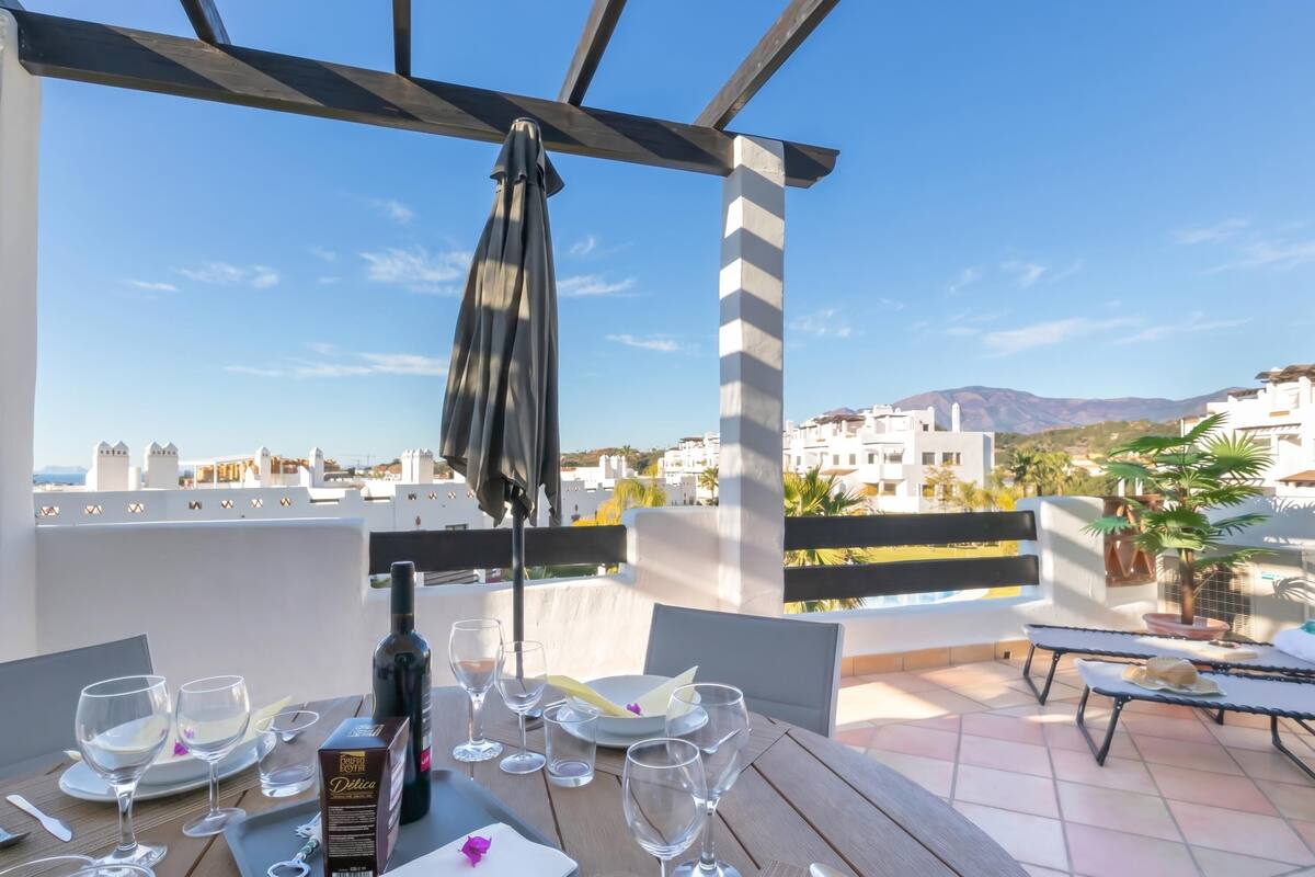Terraço com mesa posta para refeição, uma garrafa de vinho e vista para a paisagem urbana.
