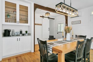 A dining area with a wooden table, black chairs, and a checkered table runner. There is a coffee station with a coffee maker and mugs.