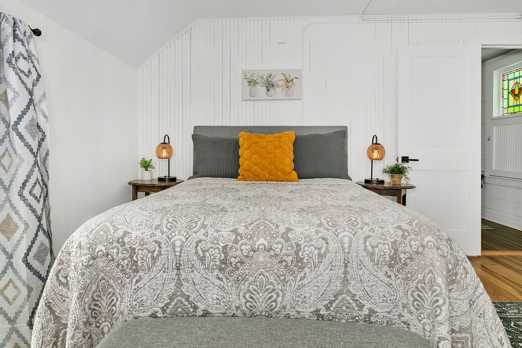 A bedroom with a patterned bedspread, a grey headboard, and two bedside lamps.