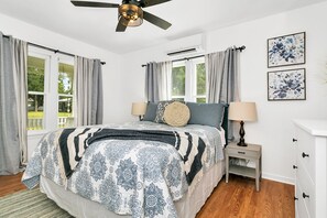 A bedroom with a bed, a nightstand, a dresser, a ceiling fan, and two windows with curtains.