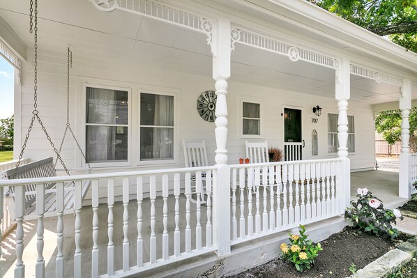 A white porch with a swing, a clock, and a door marked with the number 707.