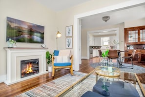 A living room with a fireplace, a TV mounted above it, and a dining area with a table and chairs.