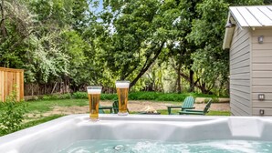 A hot tub with two glasses of beer, surrounded by greenery and a wooden deck.