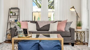 A living room with a grey sofa, blue cushions, a wooden coffee table, a floor lamp, and a bookshelf with decorative items.