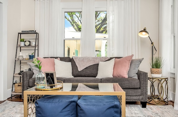 A living room with a grey sofa, blue cushions, a wooden coffee table, a floor lamp, and a bookshelf with decorative items.