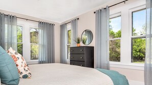 A bedroom with a bed, a dresser, and a window with curtains.