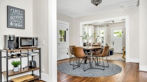 A dining area with a round table, chairs, and a coffee machine on a shelf.