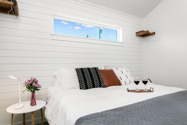 Ein Schlafzimmer mit einem Bett, einem kleinen Tisch mit Blumen und einem Fenster mit Blick zum Himmel.