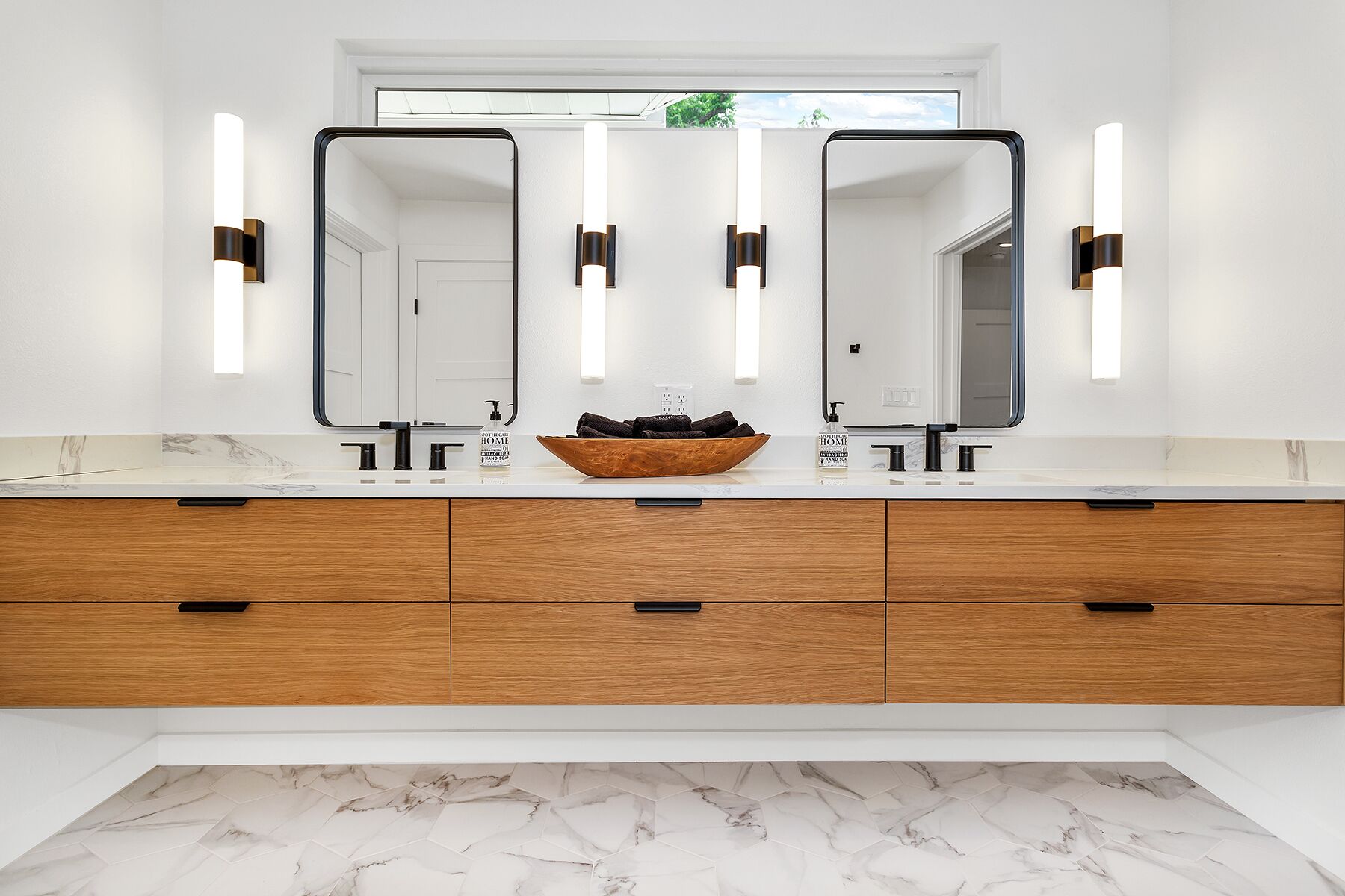 A modern bathroom with a double vanity, two mirrors, and a wooden vanity with drawers.