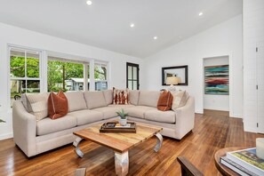 A modern living room with a sectional sofa, a wooden coffee table, and a large window offering a view of a house and greenery.