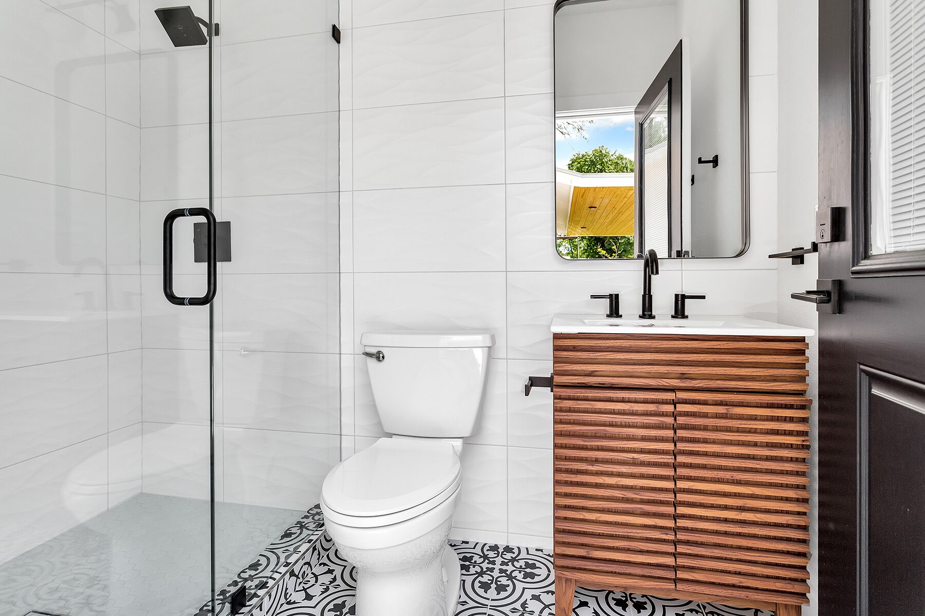 Een moderne badkamer met toilet, een wastafel met houten meubel en een douchecabine van glas.