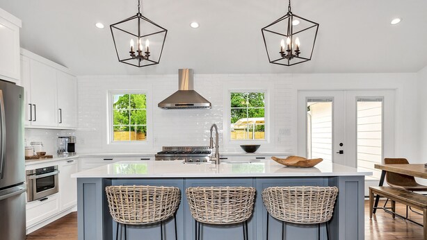 Una cocina moderna con armarios blancos, una isla central con taburetes altos e iluminación colgante.