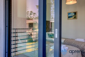 Une chambre d’hôtel moderne avec une porte vitrée donnant sur un balcon, un tableau au mur et un lit recouvert d’une couverture à motifs.