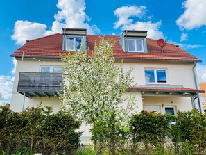 A two-story building with a red-tiled roof, dormer windows, and a balcony. - Ferienwohnung Dorfblick - Ferienhof Stephanus (Ebermannstadt)