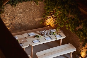 Un espace de restauration en plein air, avec un mur de pierres apparentes créant une ambiance rustique, des bancs en bois et une table dressée pour un repas.