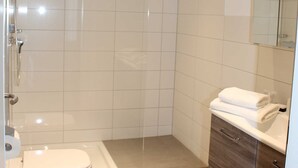 Un baño moderno con ducha acristalada, inodoro y tocador con espejo.