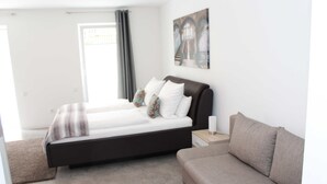 Un dormitorio moderno con cama, sofá, mesita de noche y un cuadro en la pared.
