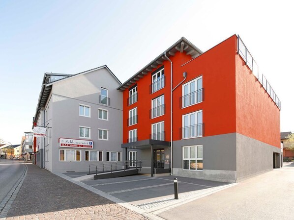 Un hotel moderno con fachada roja y gris, múltiples ventanales y una entrada visible.