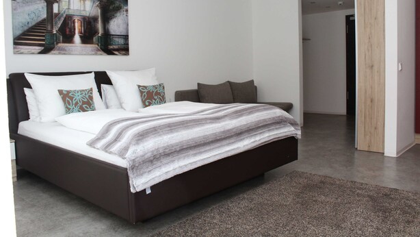 Un dormitorio moderno con una cama grande, un cuadro sobre la cama y una puerta de madera al fondo.
