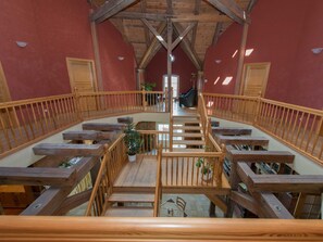 Um interior espaçoso com escada de madeira que dá acesso a um mezanino, com corrimão de madeira e plantas em vasos.