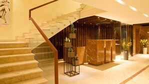 A modern hotel lobby with a marble staircase, a reception desk, and potted plants.