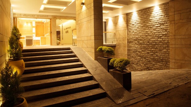 A modern hotel lobby with a staircase leading to the upper floor, featuring a stone wall and potted plants.