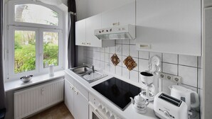 Et moderne køkken med hvide hårde hvidevarer, et vindue med udsigt til grøn natur, og et flisebeklædt backsplash.