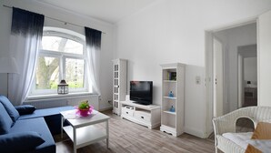 En moderne stue med sofa, TV, hvide skabe og en fletstol.