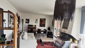 En moderne stue med sofa, sofabord og lænestole, et spiseområde med et træbord og stole, samt en pejs.