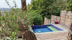 En træterrasse med jacuzzi, omgivet af frodig vegetation og et træhegn.